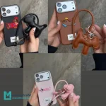 اب گوشی فانتزی طرح سگ سوسیسی با بند چرمی و چارم عروسکی متصل روی پس‌زمینه ساده.